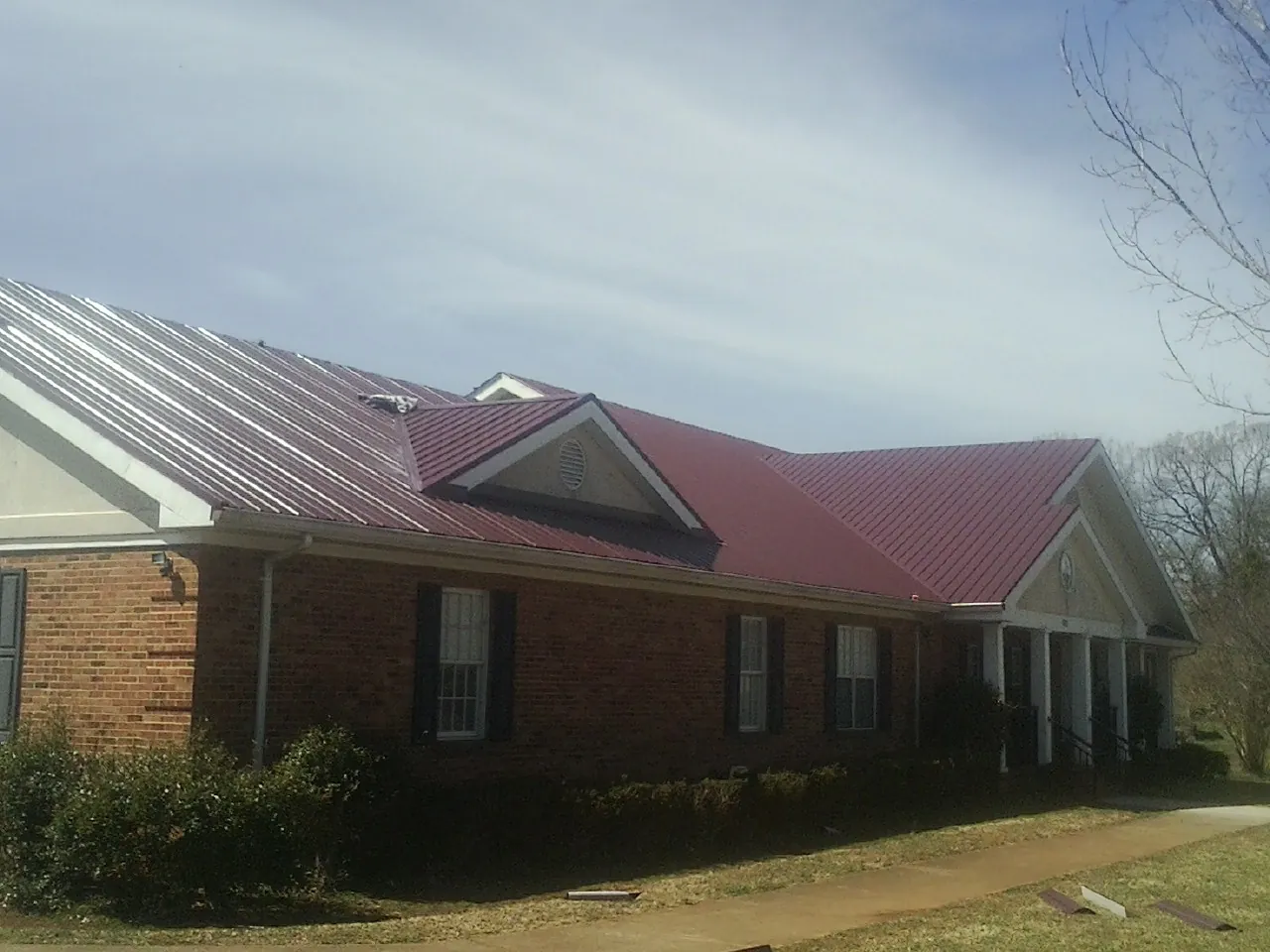 Red metal roof with gabled entries on a long brick building, from a Hail Damage Roof Repair job in Cedar City