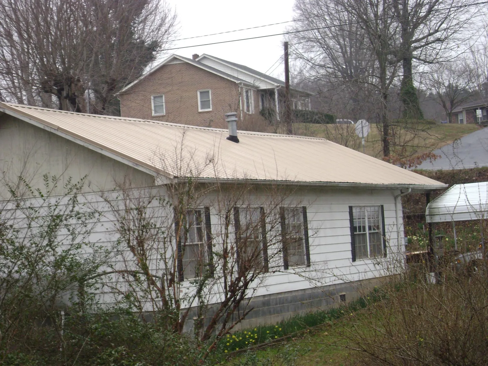 Tan metal roof on a white sided house set into a hillside — Commercial Roofing by Roofing Brothers in Cedar City